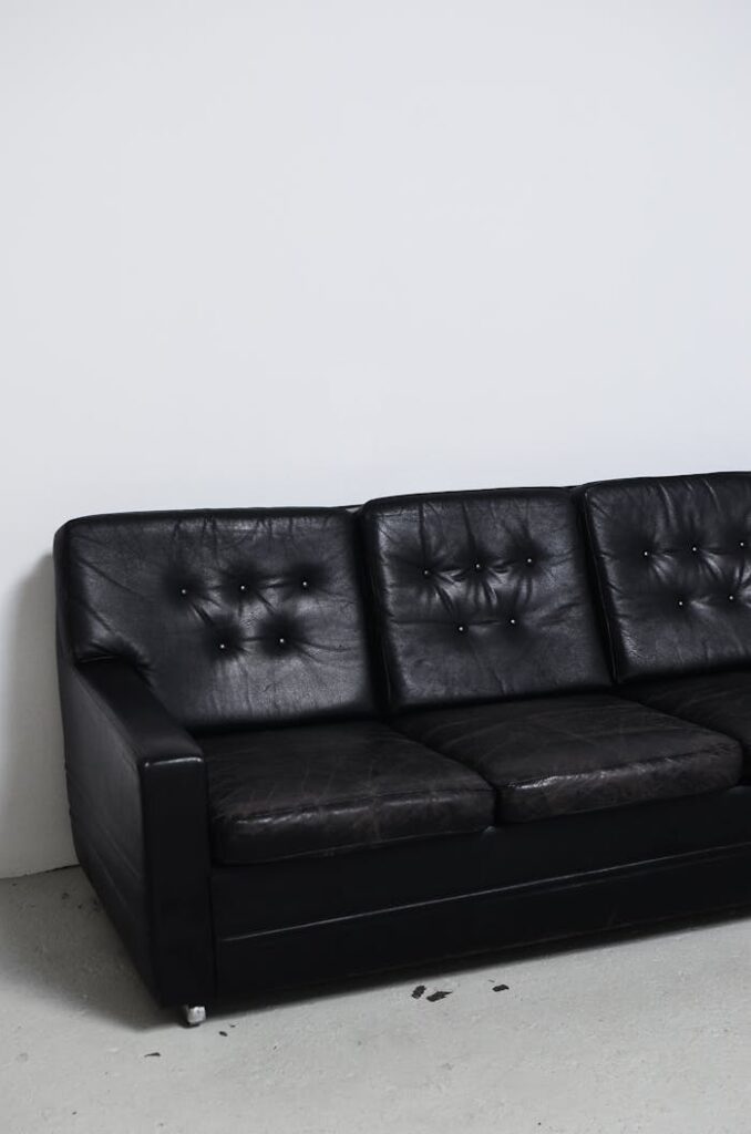 Black leather couch against a white wall in a minimalist empty room setting.